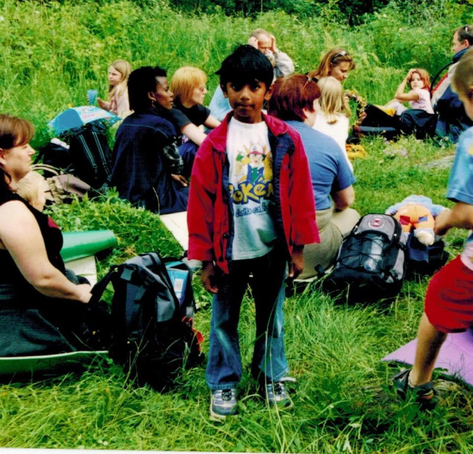 Me as a kid in a red jacket and a Pokémon shirt, standing in tall grass