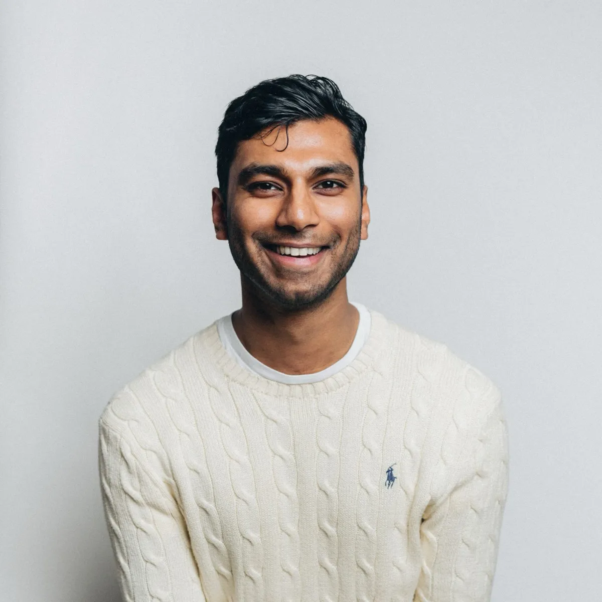 Lush smiling, in a cream cable-knit jumper against a pale grey wall